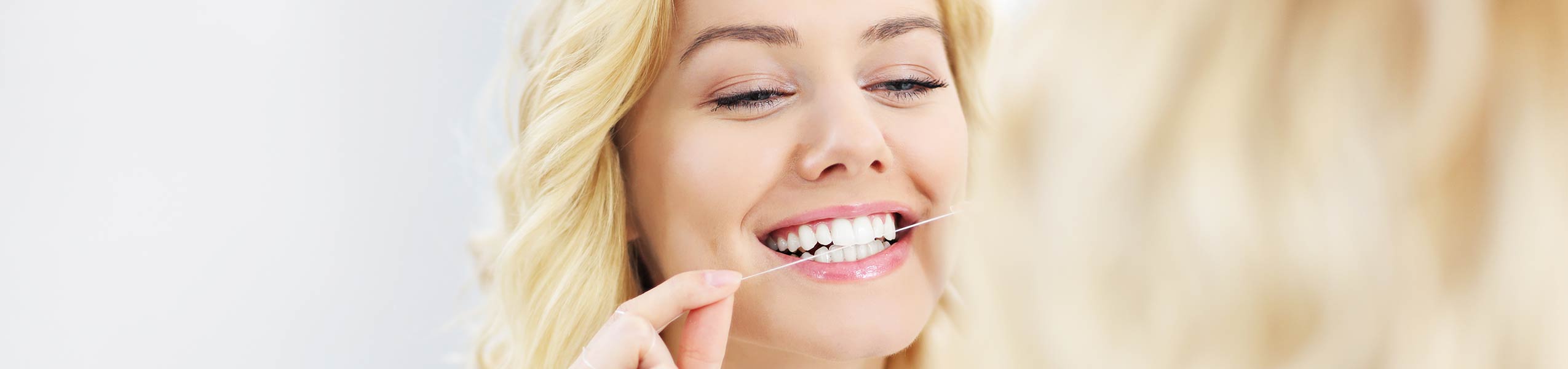 Blonde girl flossing her teeth while smiling.